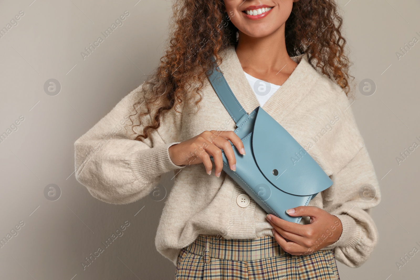 Photo of Young African American woman with stylish waist bag on beige background, closeup