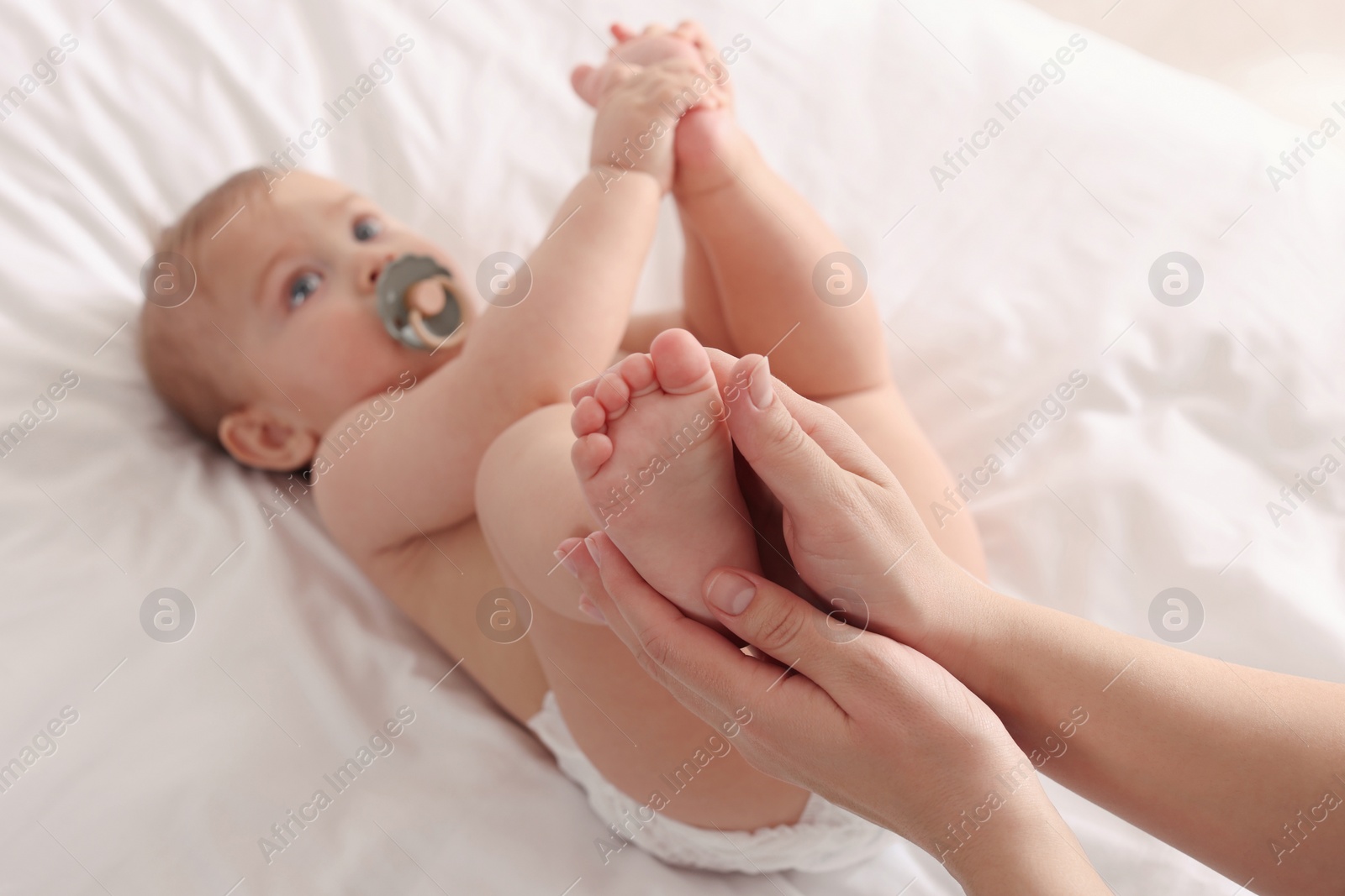 Photo of Mother massaging her cute baby with oil on bed, closeup