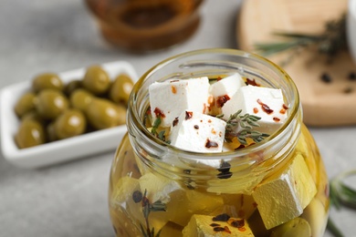 Jar with feta cheese marinated in oil on light grey table, closeup. Pickled food