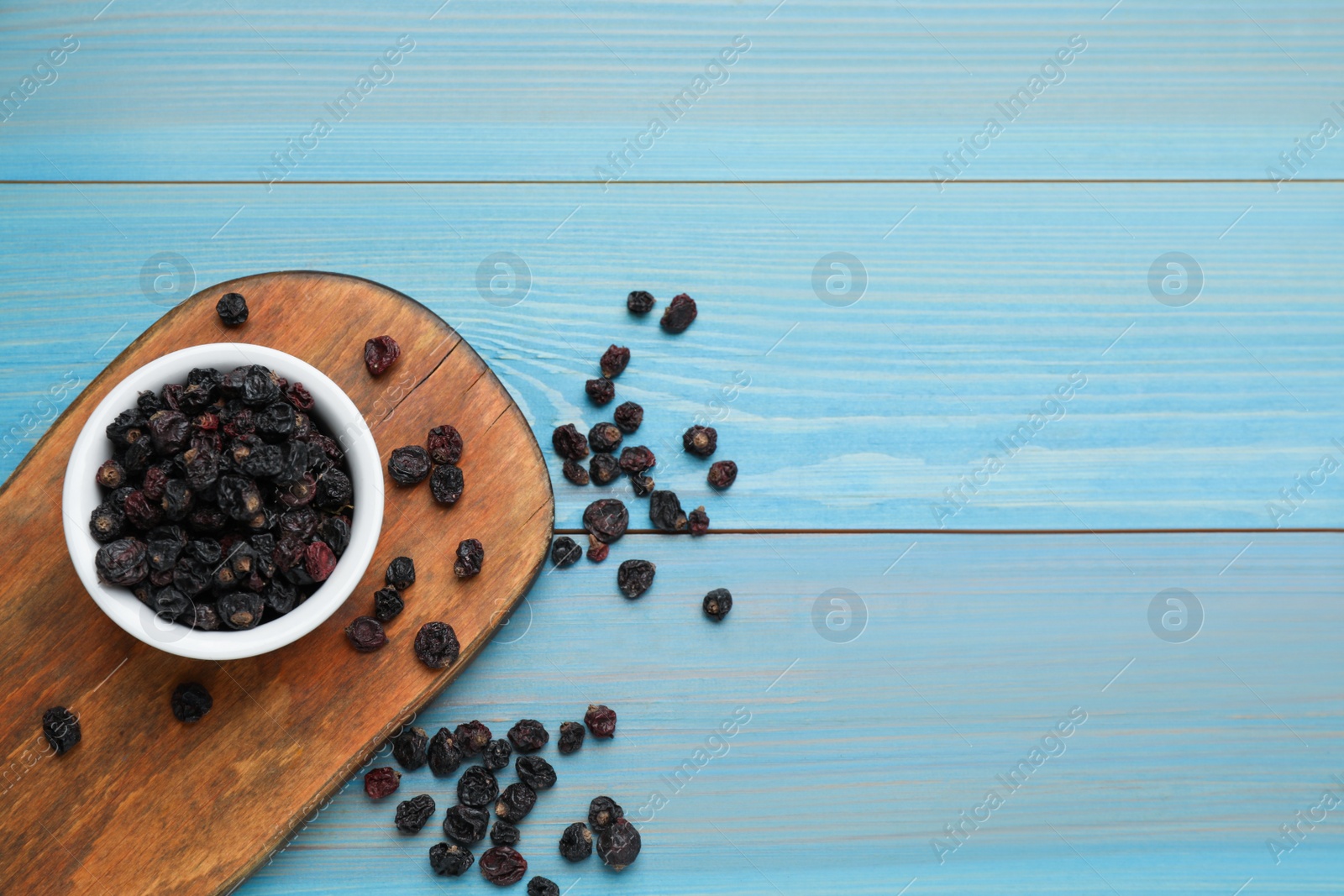 Photo of Dried black currant berries on light blue wooden table, flat lay. Space for text