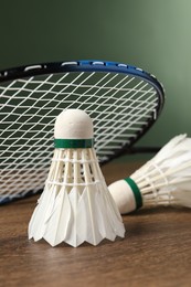 Photo of Feather badminton shuttlecocks and racket on wooden table against green background, closeup. Space for text