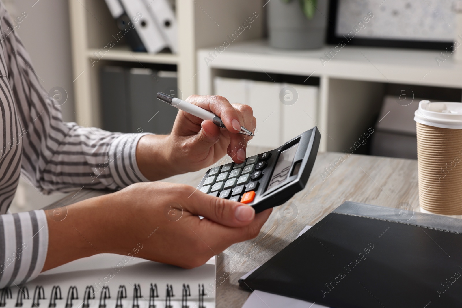 Photo of Woman using calculator at light wooden table in office, closeup