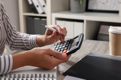 Woman using calculator at light wooden table in office, closeup