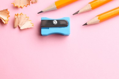 Photo of Pencils, sharpener and shavings on pale pink background, flat lay. Space for text