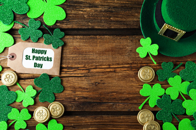 Photo of Frame made of clover leaves, gold coins and leprechaun hat on wooden table, flat lay with space for text. St. Patrick's Day celebration