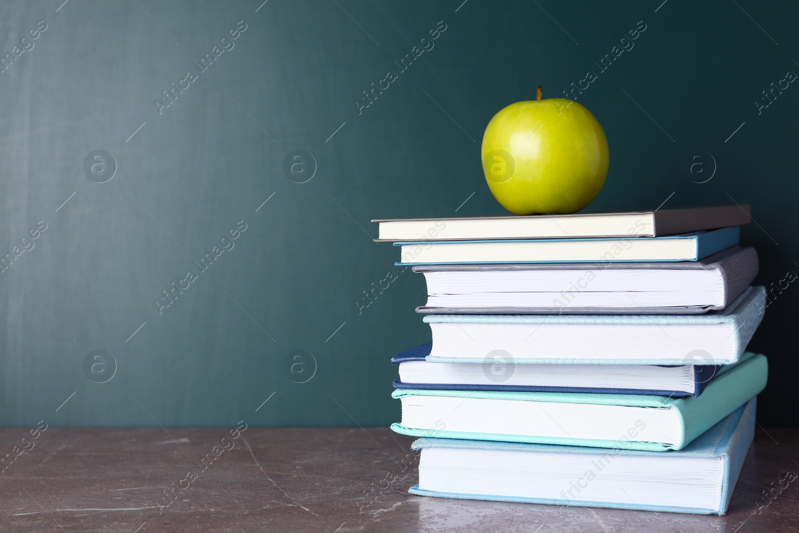 Photo of Books and apple on grey table near chalkboard, space for text. School education