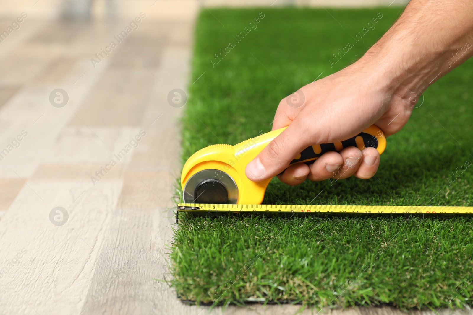 Photo of Man cutting artificial grass carpet indoors, closeup. Space for text