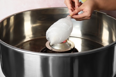 Photo of Young woman making cotton candy with modern machine on pink background, closeup