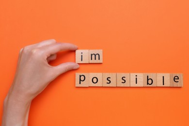 Photo of Motivation concept. Woman changing word from Impossible into Possible by removing wooden squares on orange background, top view