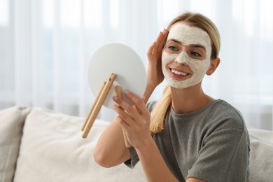 Photo of Young woman with face mask looking into mirror indoors. Spa treatments