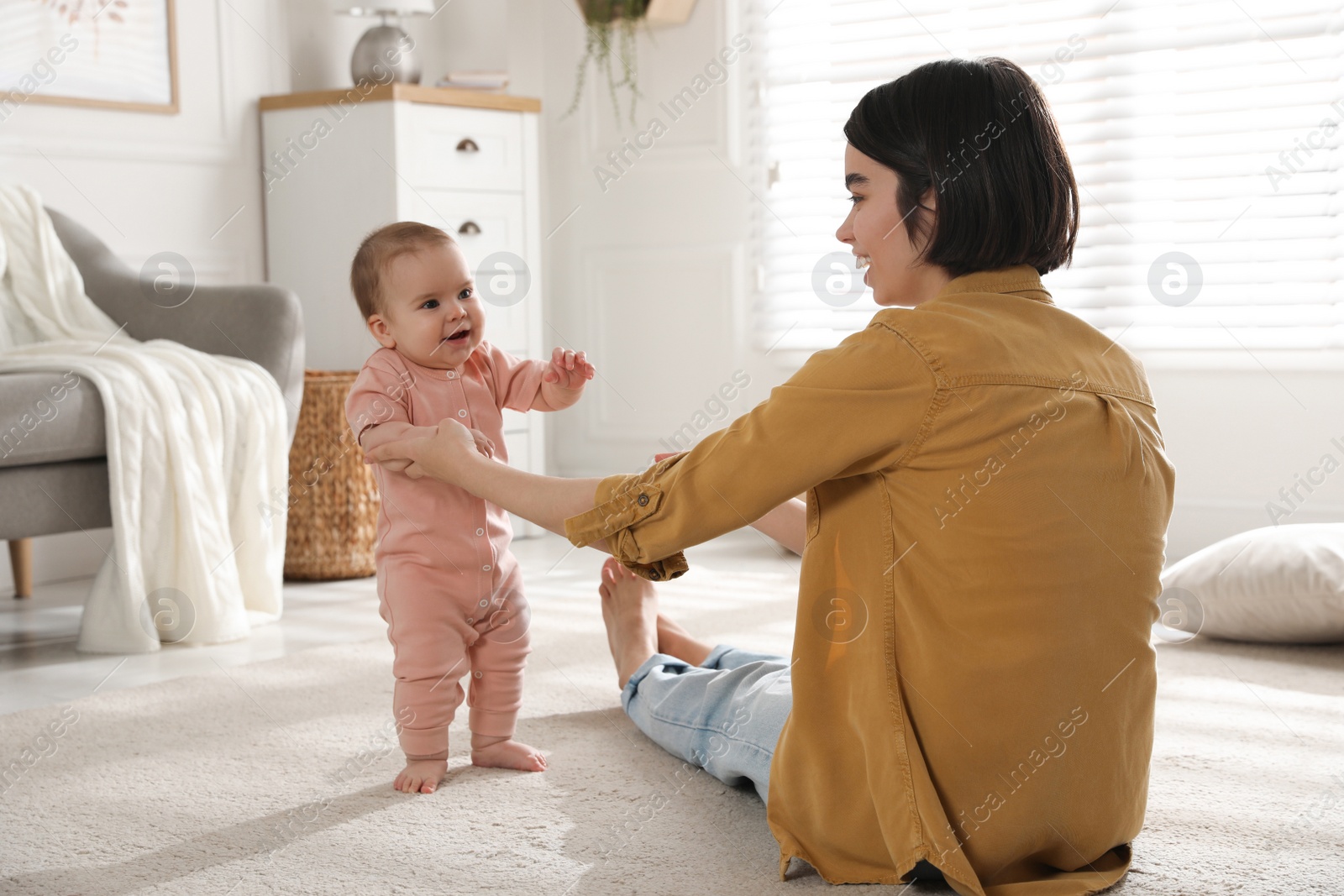 Photo of Mother supporting her baby daughter while she learning to walk at home