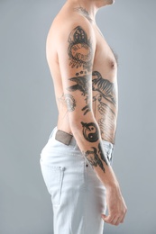 Young man with stylish tattoos on grey background