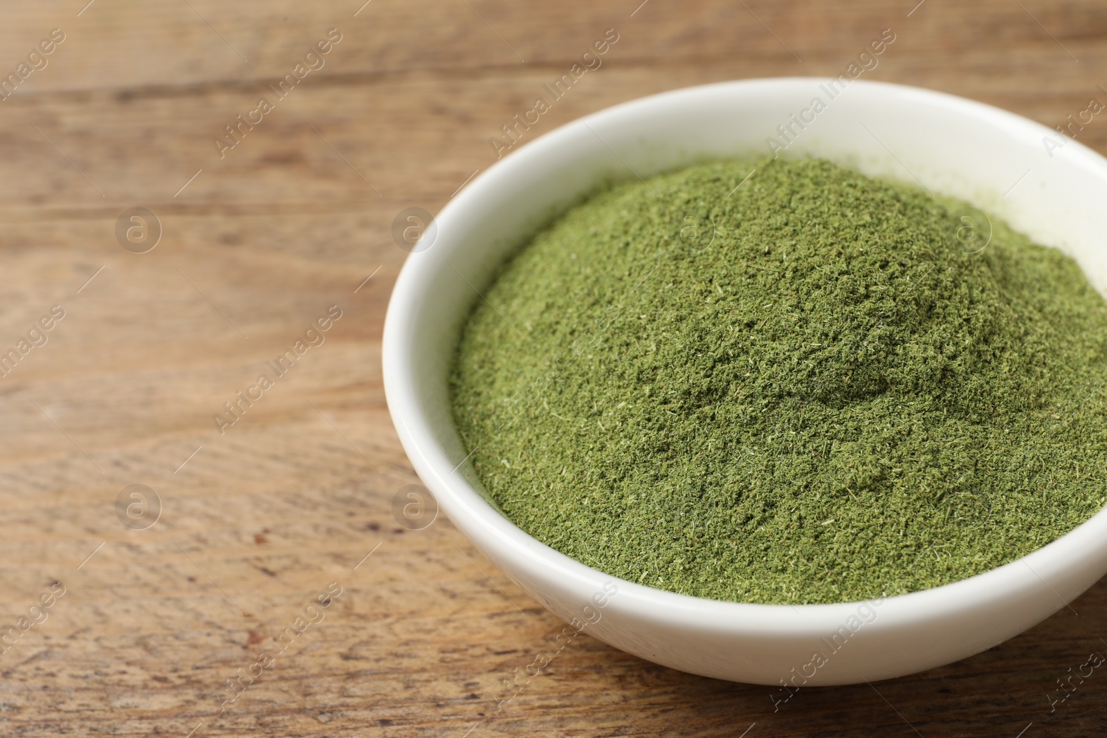 Photo of Wheat grass powder in bowl on wooden table, closeup. Space for text