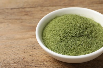 Wheat grass powder in bowl on wooden table, closeup. Space for text