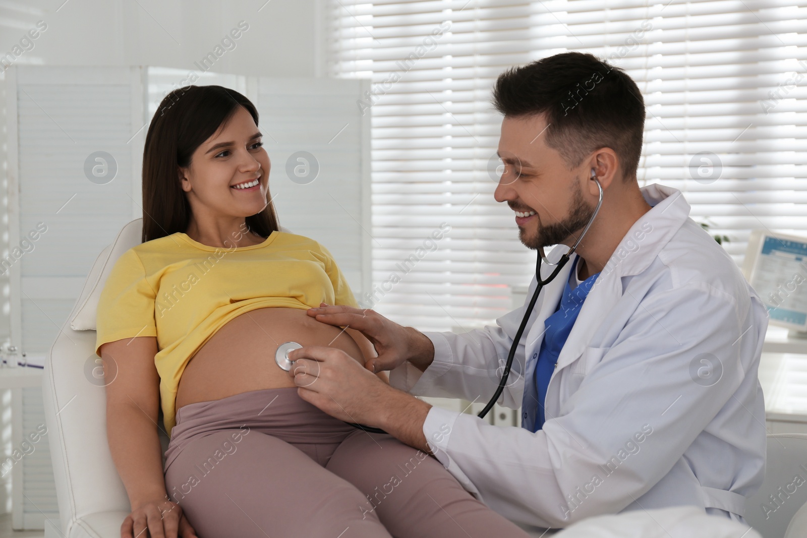 Photo of Doctor examining pregnant woman with stethoscope in clinic