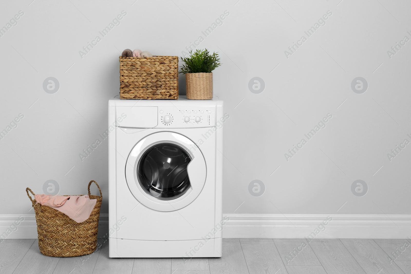 Photo of Modern washing machine with houseplant and laundry baskets near white wall. Space for text