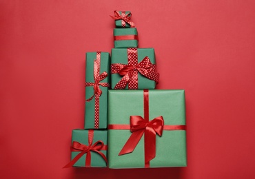 Photo of Christmas tree shape of gift boxes on red background, flat lay