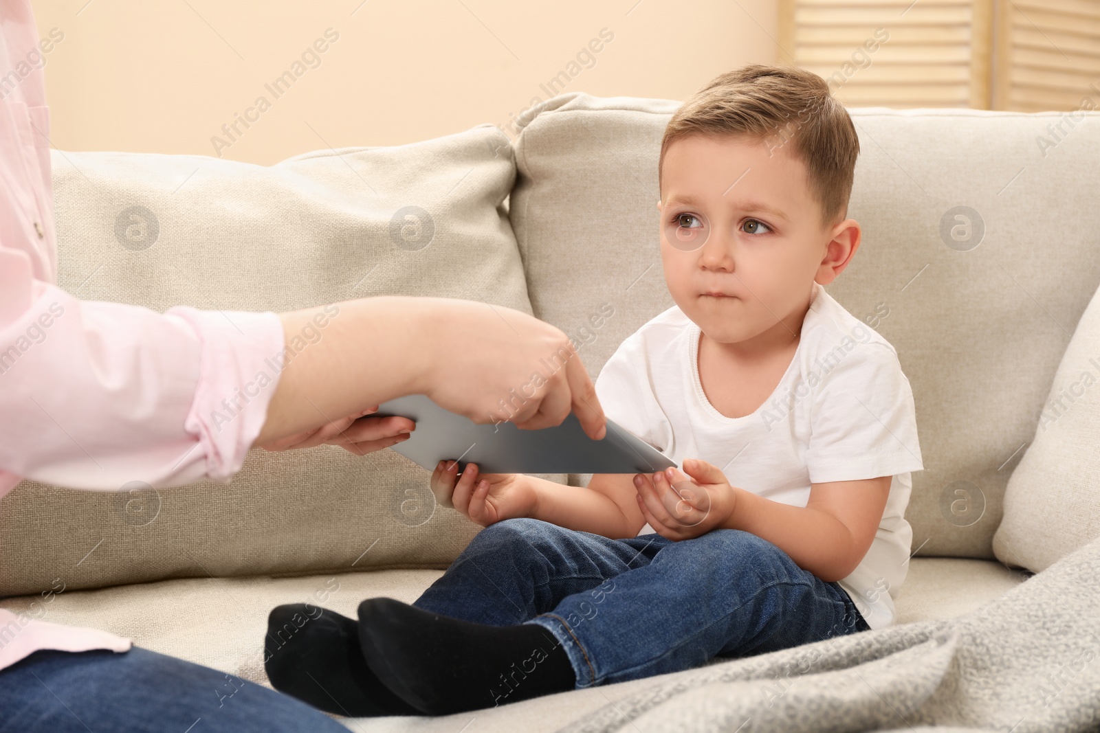 Photo of Internet addiction. Mother taking away tablet from her little son on sofa at home, closeup