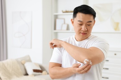 Photo of Handsome man applying body cream onto his elbow at home, space for text