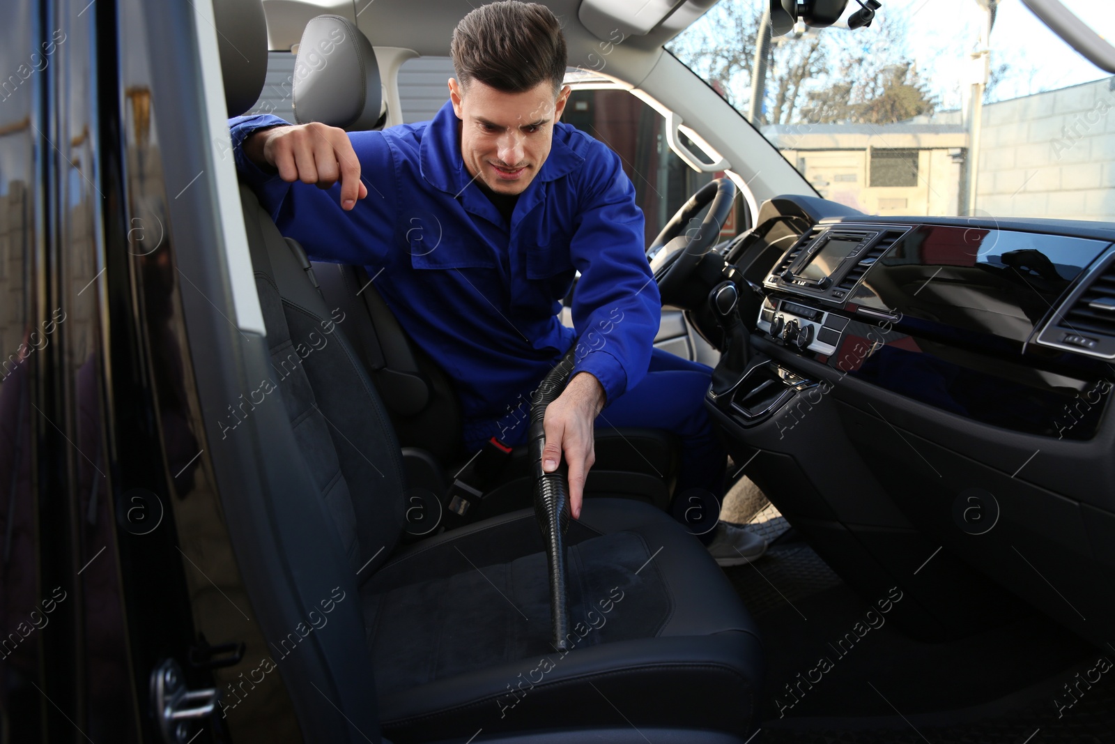 Photo of Car wash worker vacuuming upholstery on automobile seat