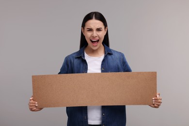 Photo of Angry woman holding blank cardboard banner on grey background, space for text