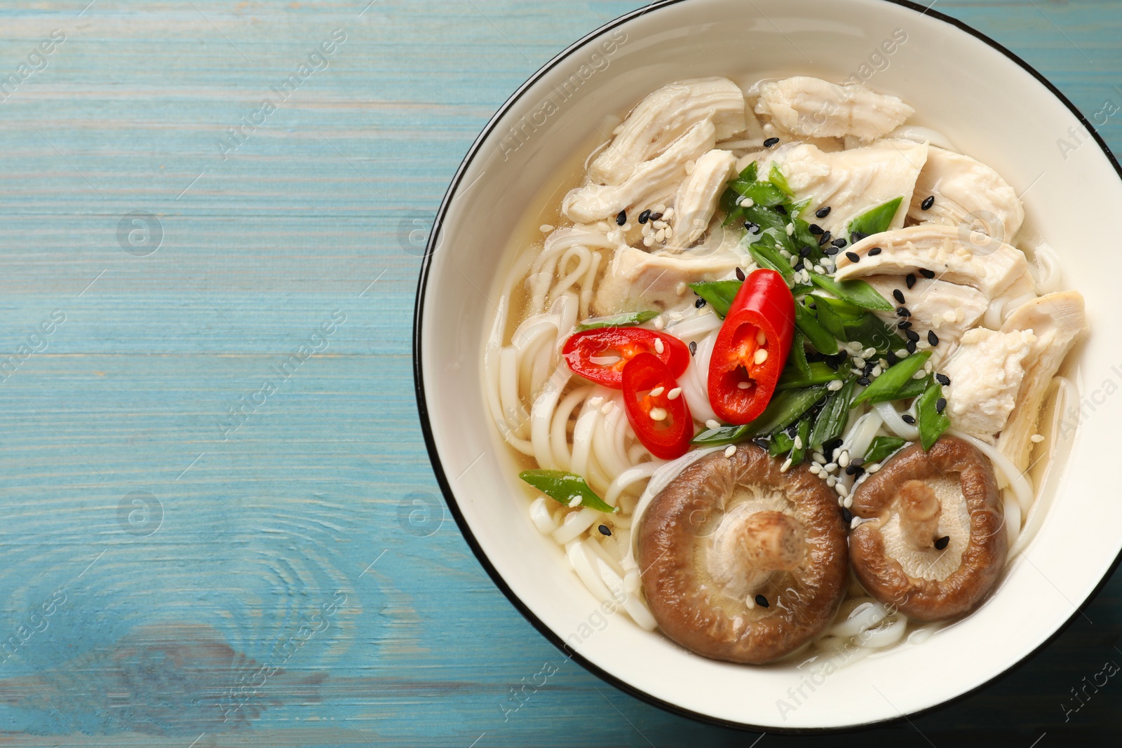 Photo of Delicious ramen with meat and mushrooms in bowl on light blue wooden table, top view. Space for text