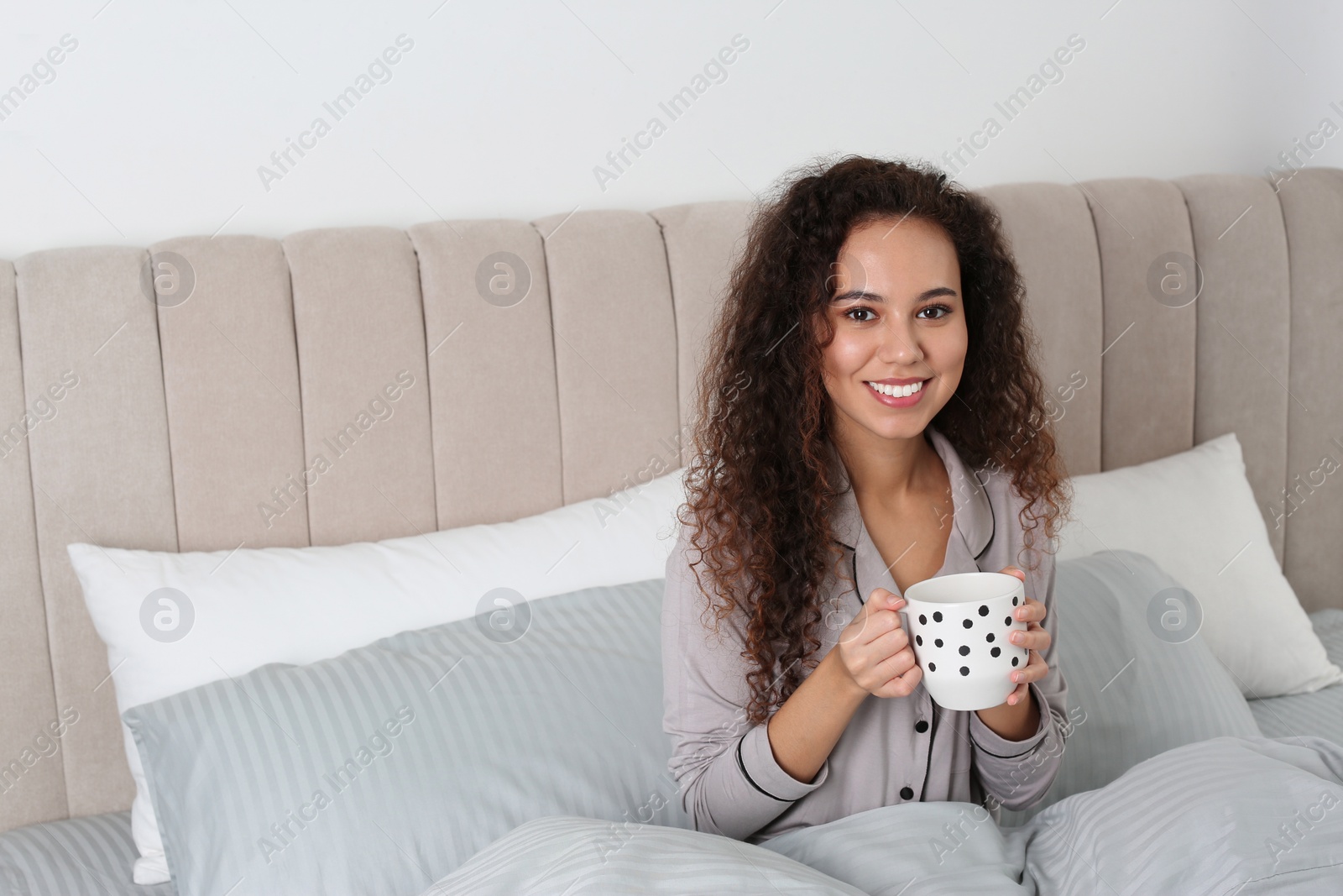 Photo of Beautiful African American woman with cup of drink in bed at home