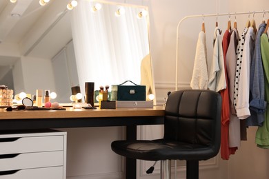 Photo of Makeup room. Stylish dressing table with mirror, chair and clothes rack