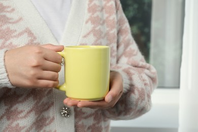 Photo of Woman holding yellow mug indoors, closeup. Mockup for design