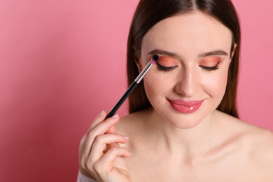 Photo of Beauty blogger applying eyeshadow on pink background, closeup