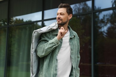 Photo of Attractive happy man holding garment cover with clothes outdoors. Dry cleaning service