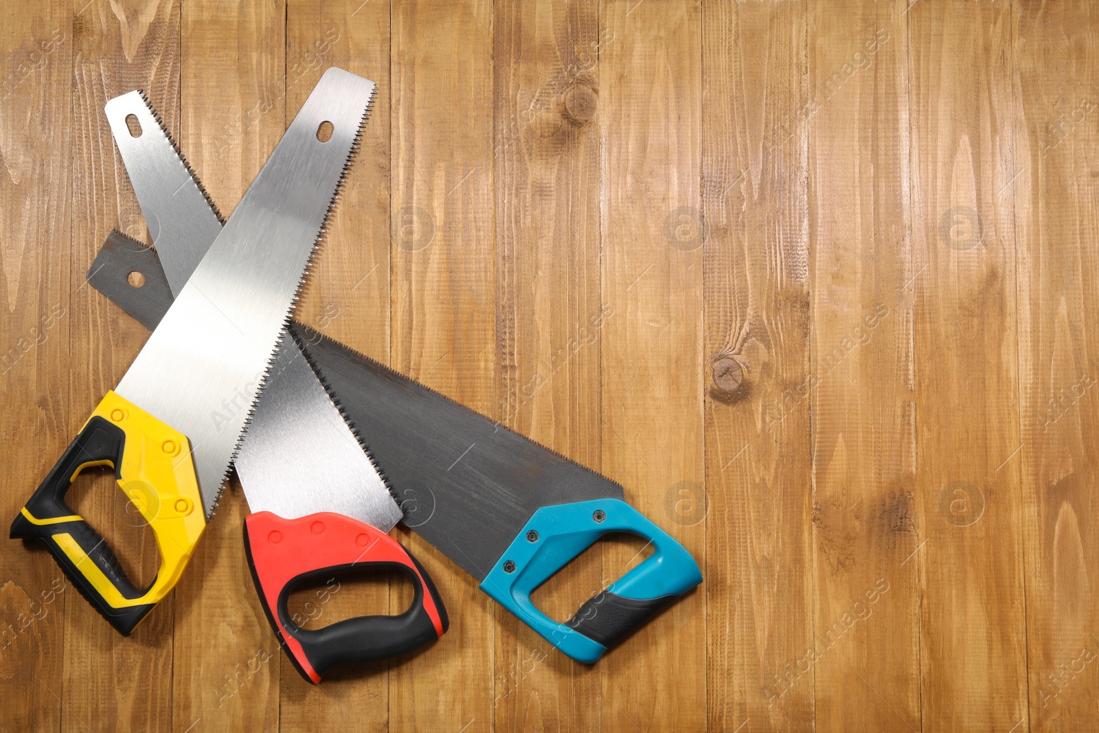 Photo of Saws with colorful handles on wooden background, flat lay. Space for text