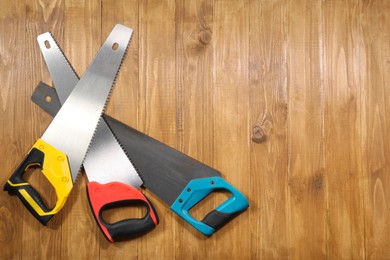 Saws with colorful handles on wooden background, flat lay. Space for text