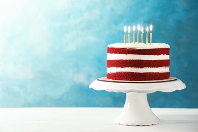 Delicious homemade red velvet cake with candles on table against color background. Space for text