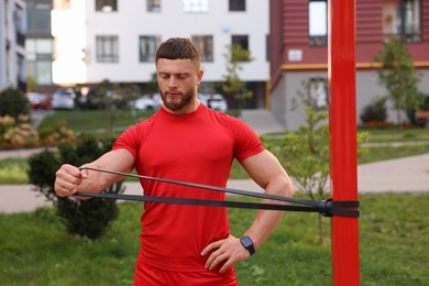 Photo of Muscular man doing exercise with elastic resistance band outdoors