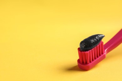 Photo of Brush with charcoal toothpaste on yellow background. Space for text