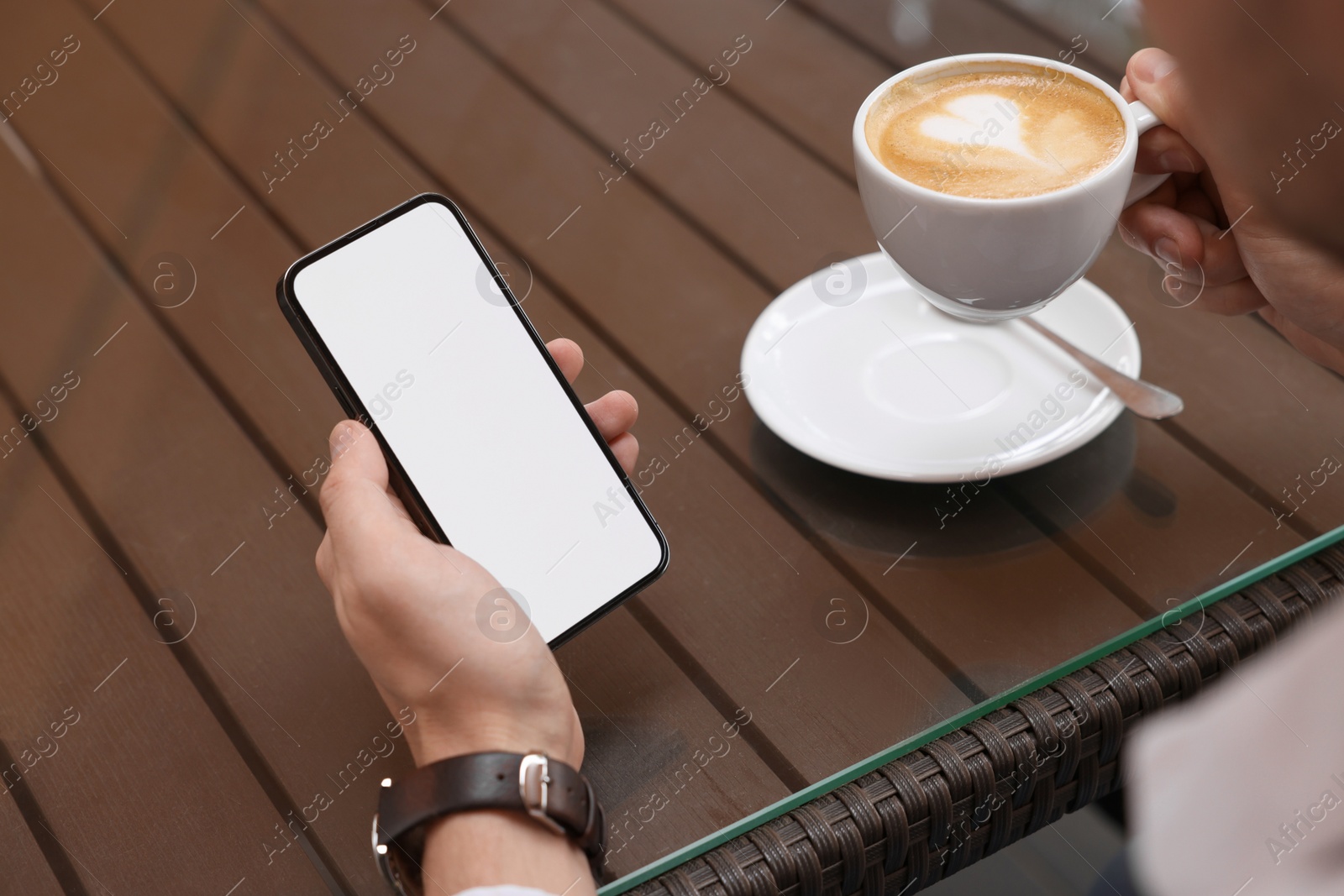 Photo of Man with cup of drink using mobile phone at table outdoors, closeup