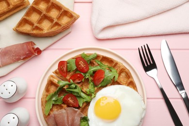 Photo of Fresh Belgian waffles with fried egg, arugula, tomatoes and jamon served for breakfast on pink wooden table, flat lay