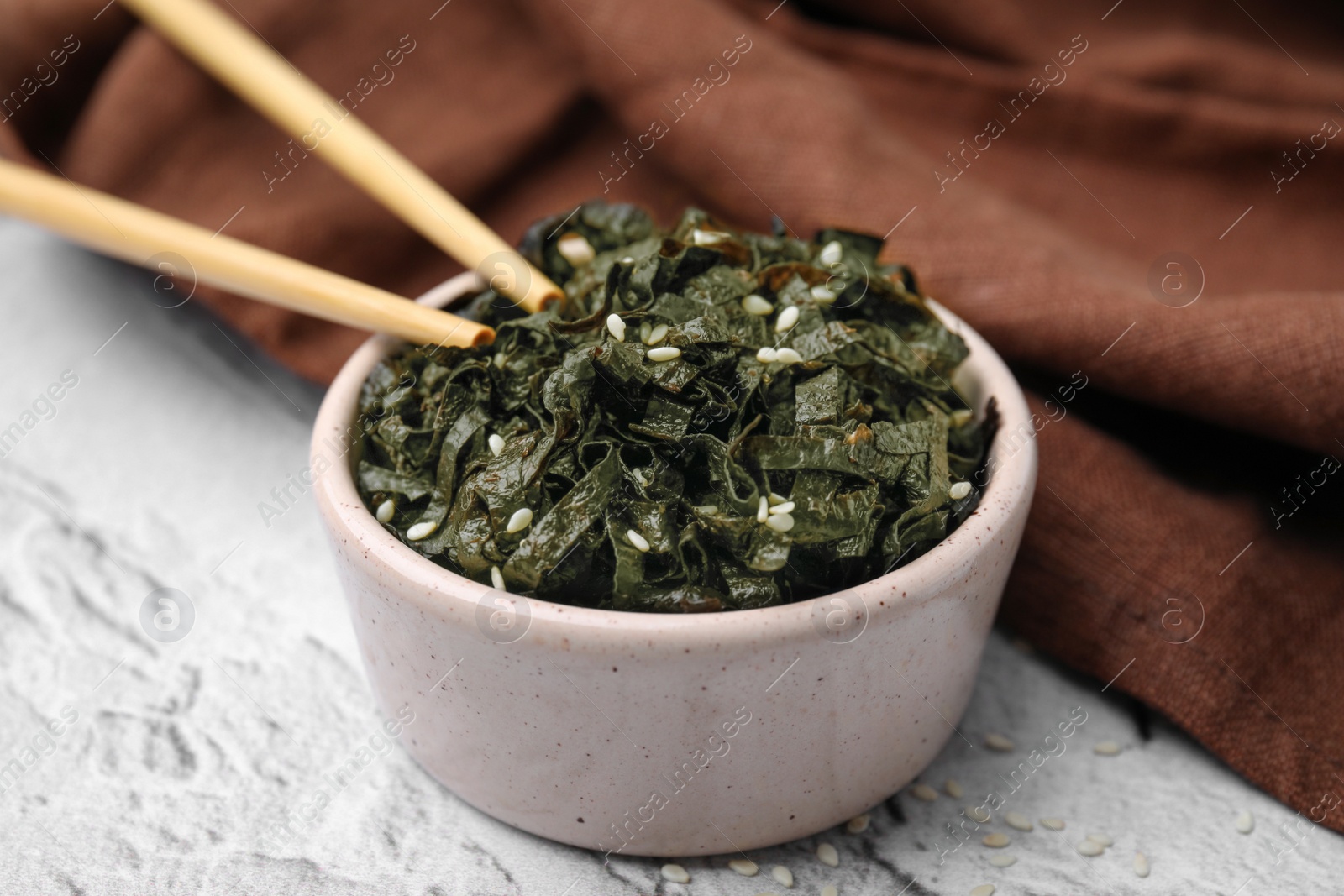 Photo of Chopped nori sheets with sesame and chopsticks on white textured table, closeup