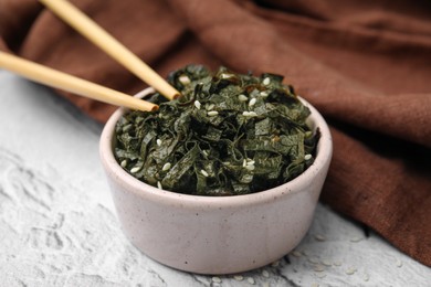 Photo of Chopped nori sheets with sesame and chopsticks on white textured table, closeup