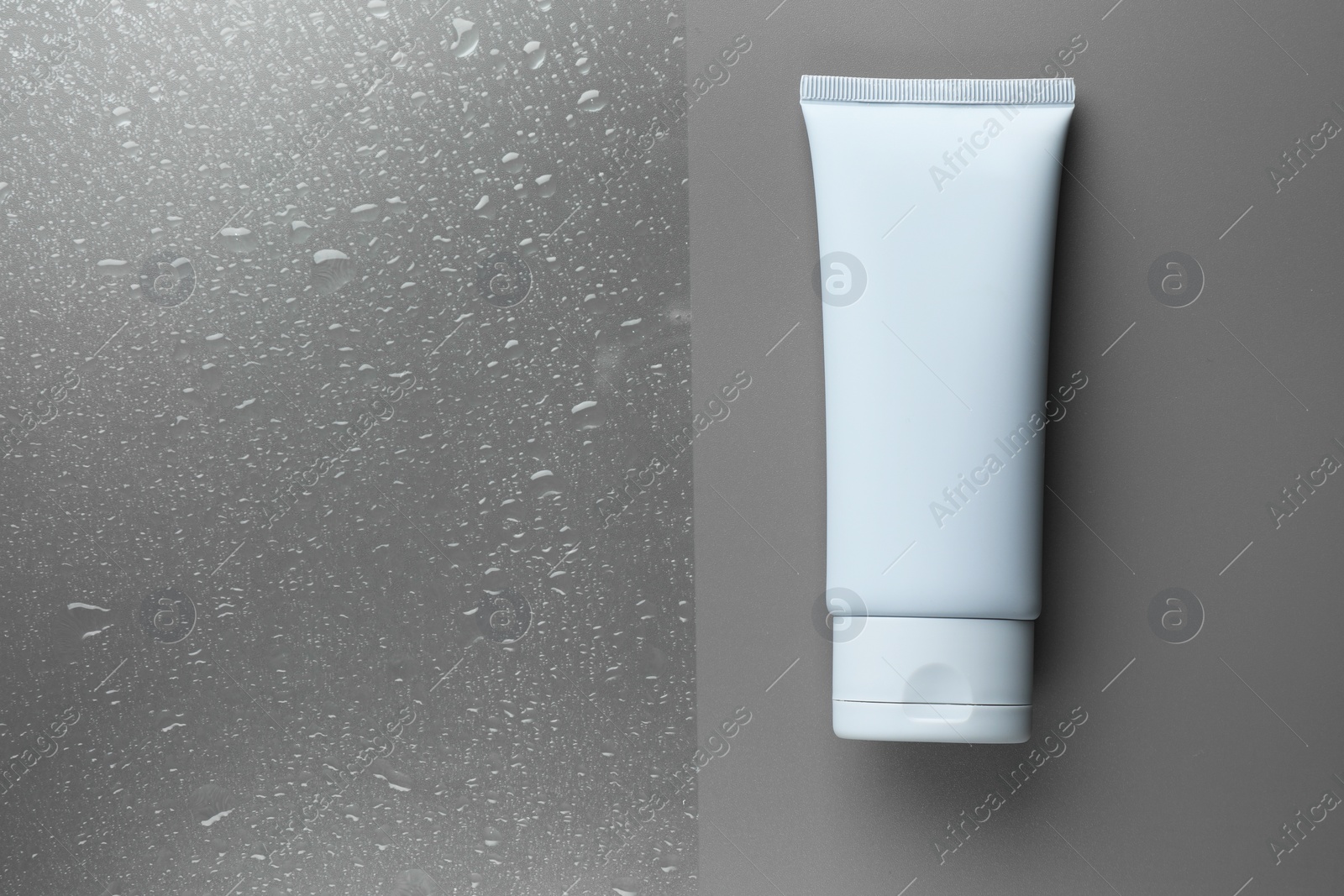 Photo of Tube with moisturizing cream on wet grey surface, top view. Space for text