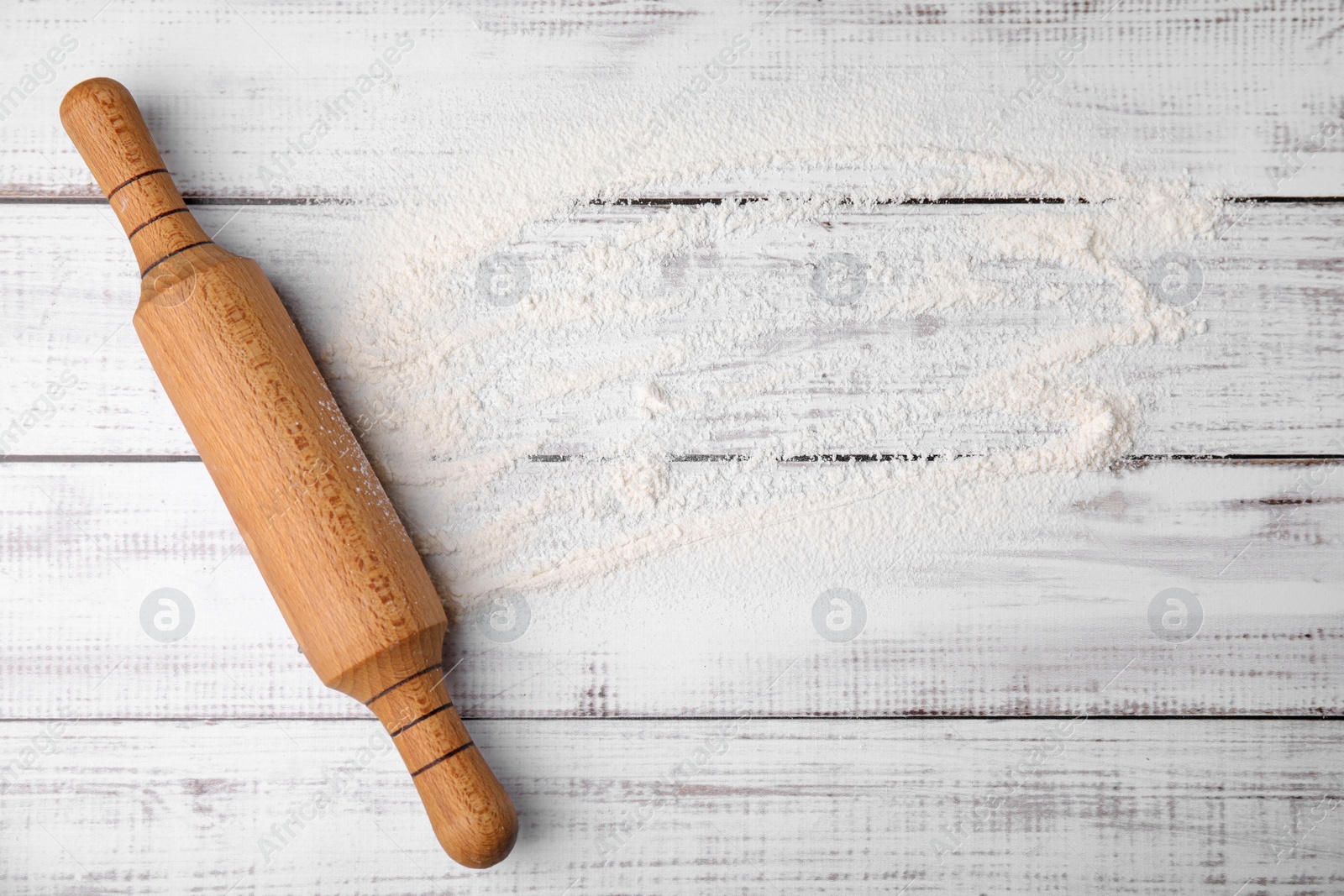 Photo of Flour and rolling pin on white wooden table, top view