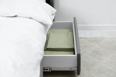 Storage drawer with bedding under modern bed in room, closeup