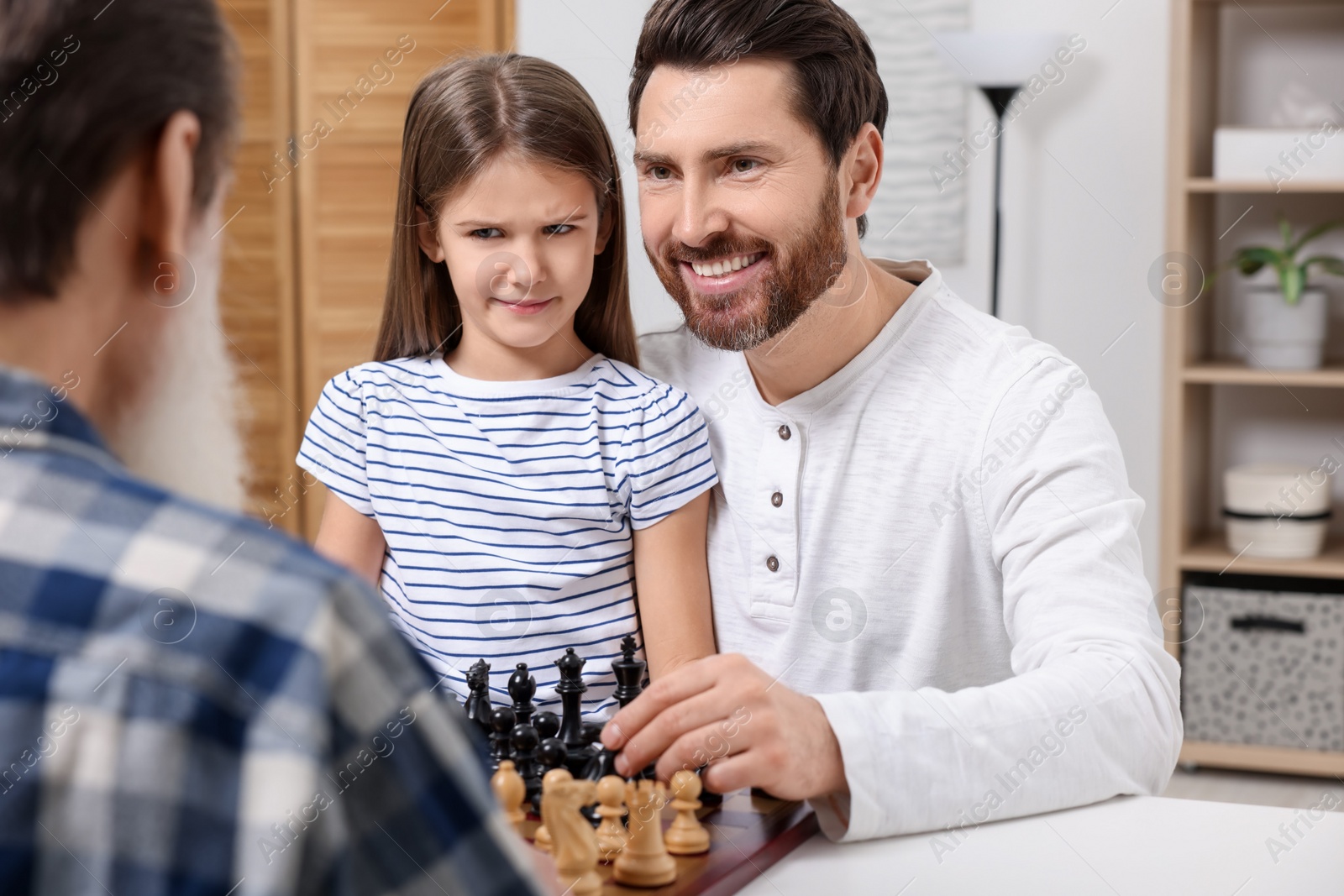 Photo of Family playing chess together at table in room