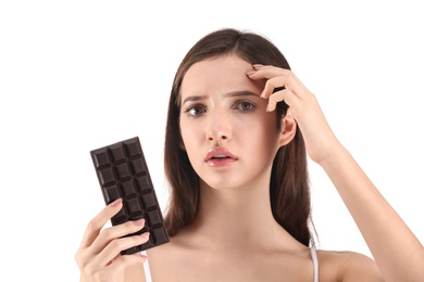Teenage girl with acne problem holding chocolate bar against white background