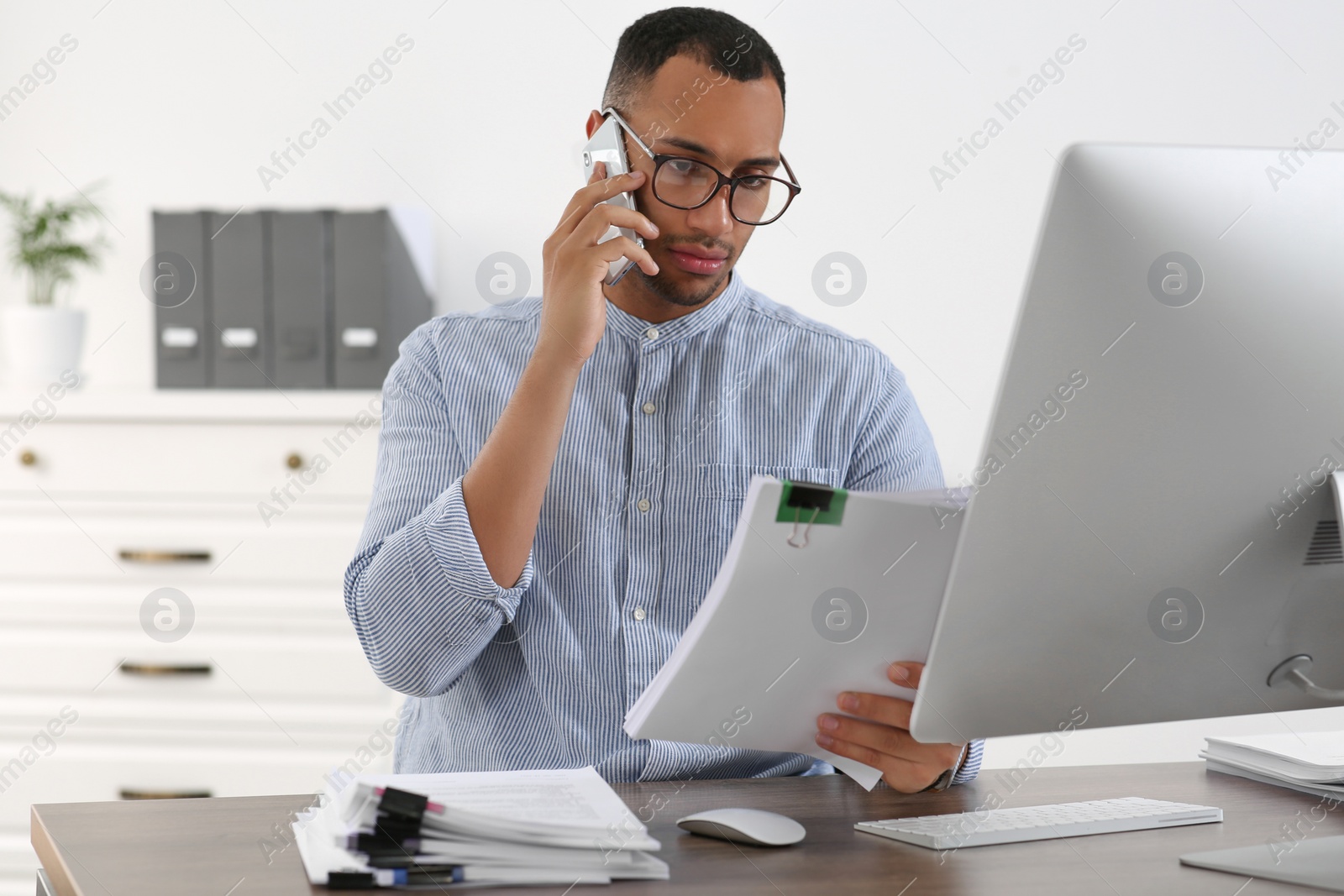 Photo of Man talking on phone while working with documents at wooden table in office