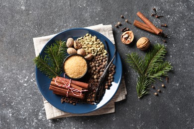 Different aromatic spices and fir branches on grey textured table, flat lay