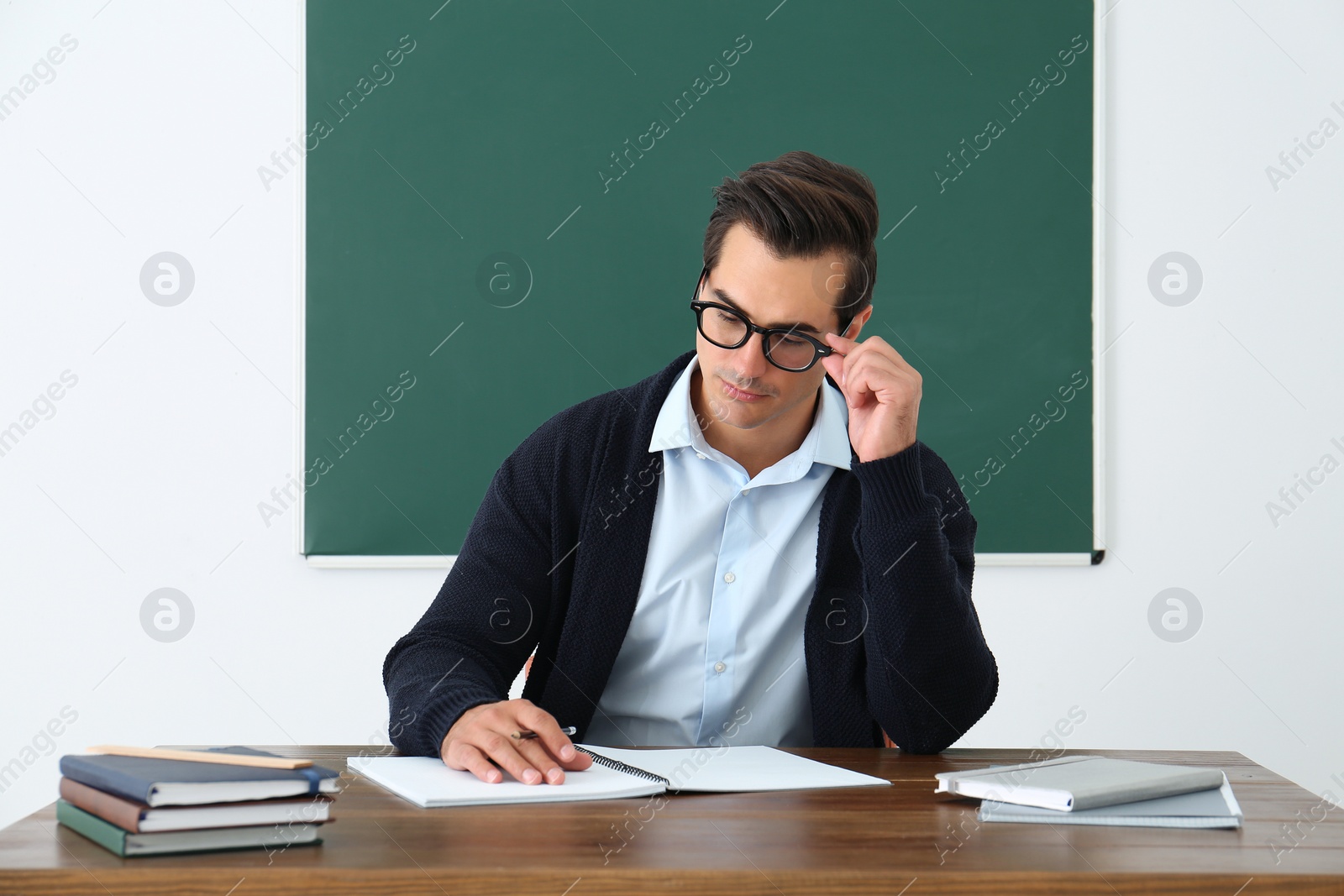 Photo of Young teacher working at table in classroom