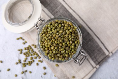 Photo of Glass jar with green mung beans on white textured table, flat lay