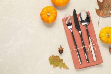 Cutlery, napkin and autumn decoration on beige marble background, flat lay with space for text. Table setting